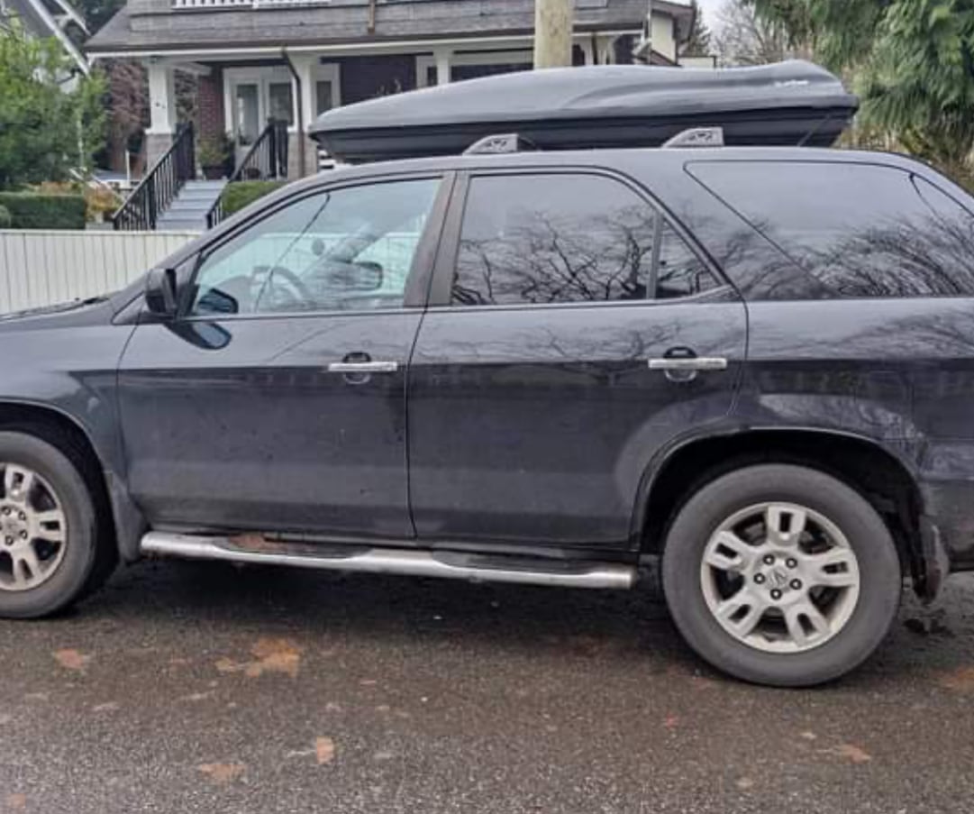 An older Acura is parked on a street in front of a house 