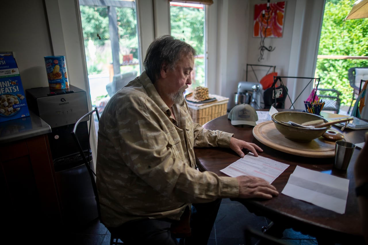 A 66 year old Surrey man looks over his vehicle registration papers in a dark kitchen.