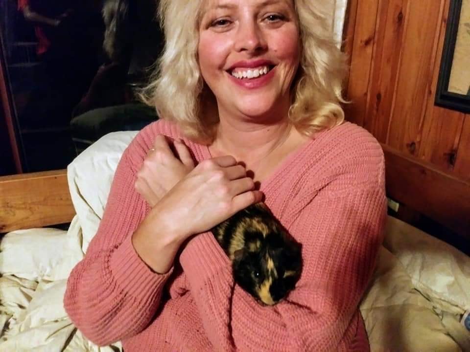 A woman carries a large rodent while smiling.