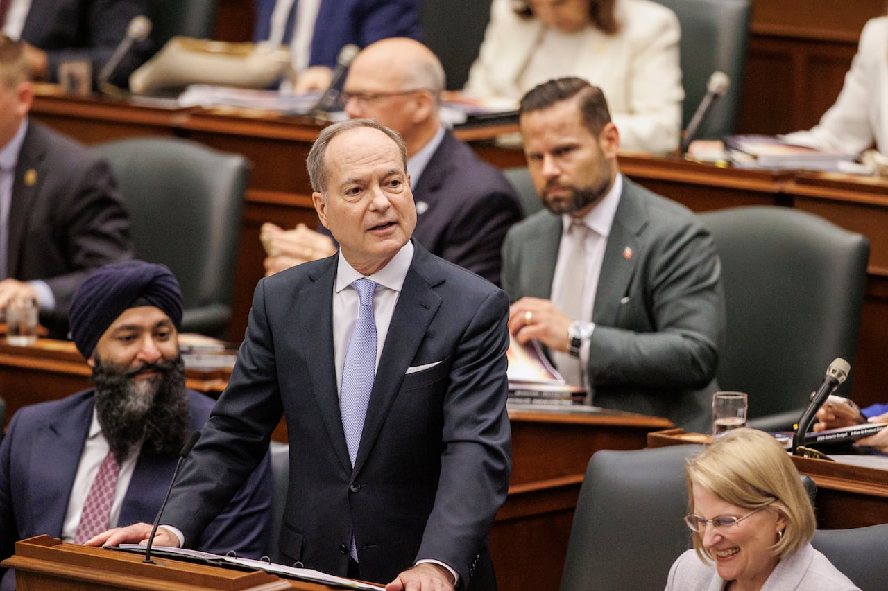 Man stands with his hands on a desk, speaking to an audience.