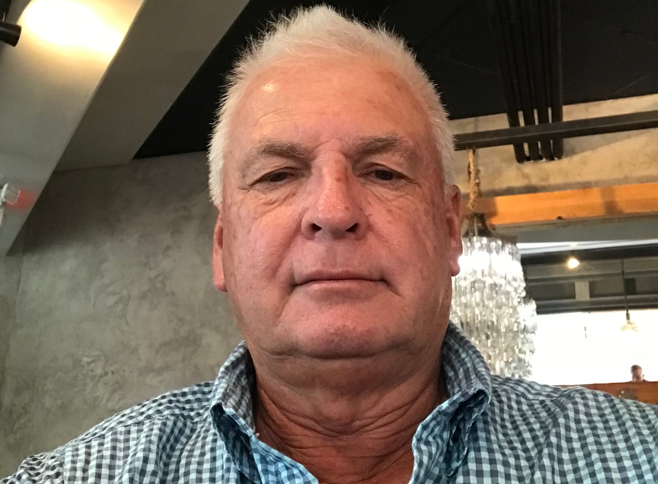 A man with short, white hair in a checked shirt takes a selfie. 
