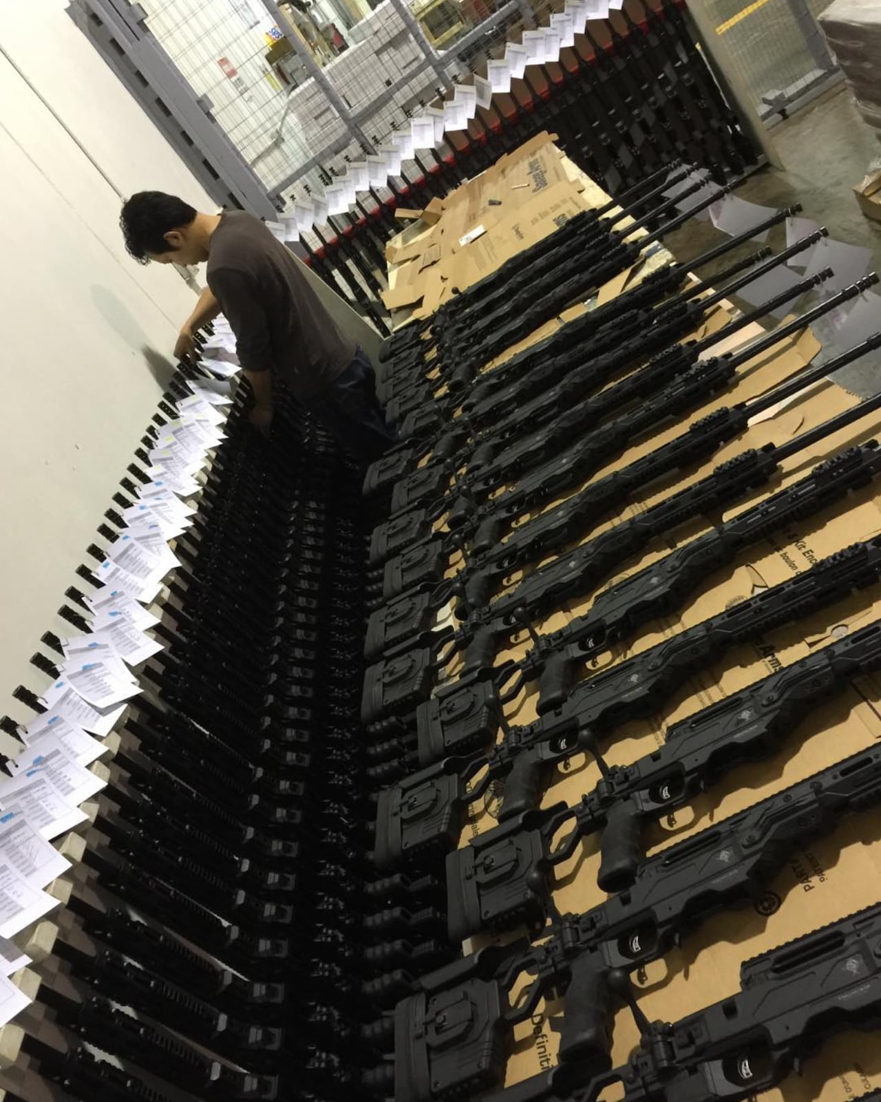 Dozens of rifles are laid out on display, with paperwork attached to the barrels. 