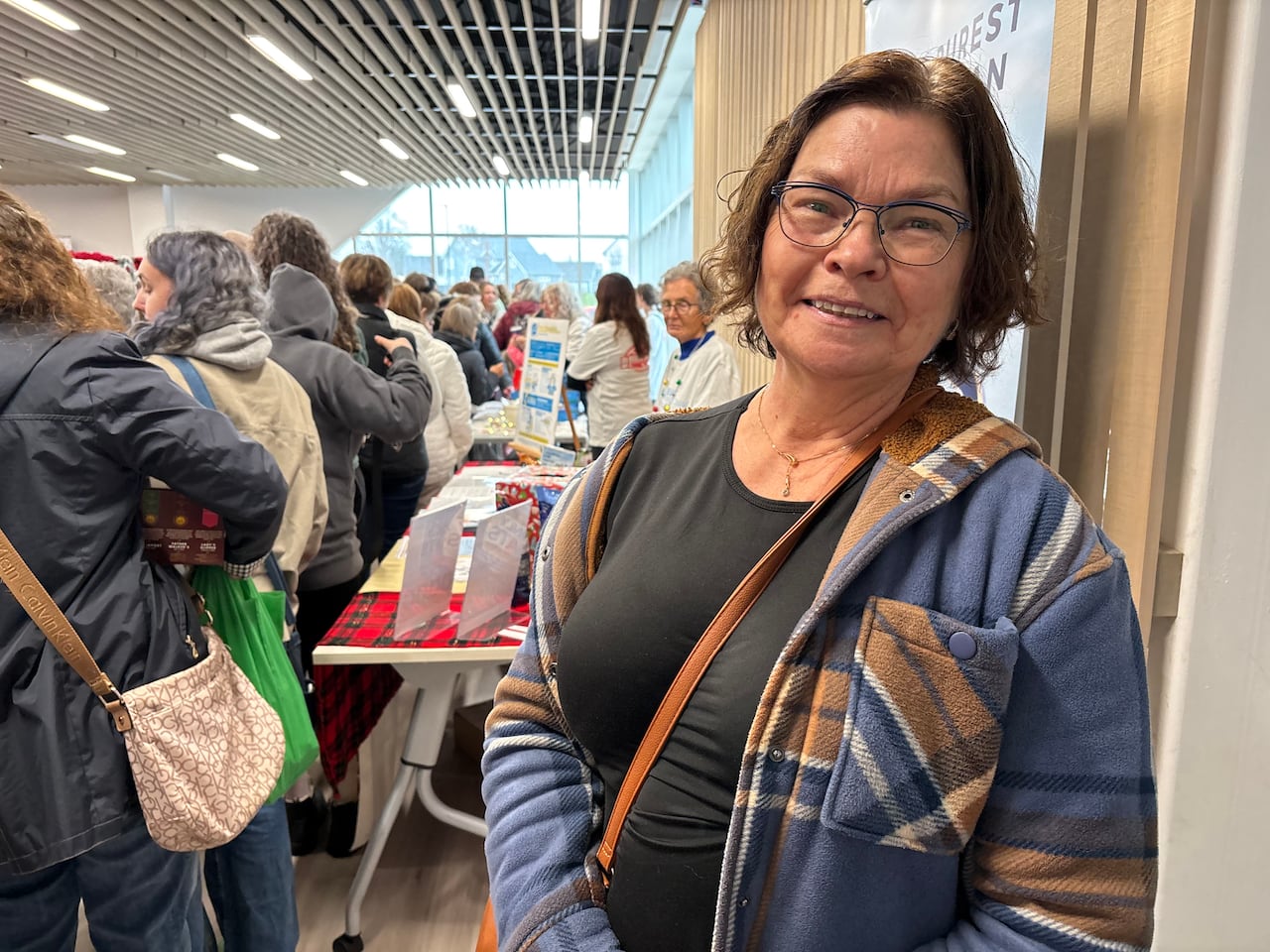 A woman wearing a plaid coat and brown purse stands in front of a table that is selling products