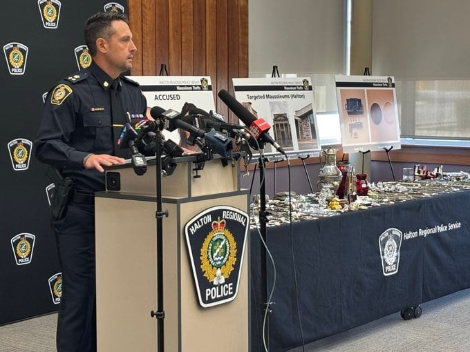 A man in police uniform speaks at a mic stand with a table behind him with many items displayed.