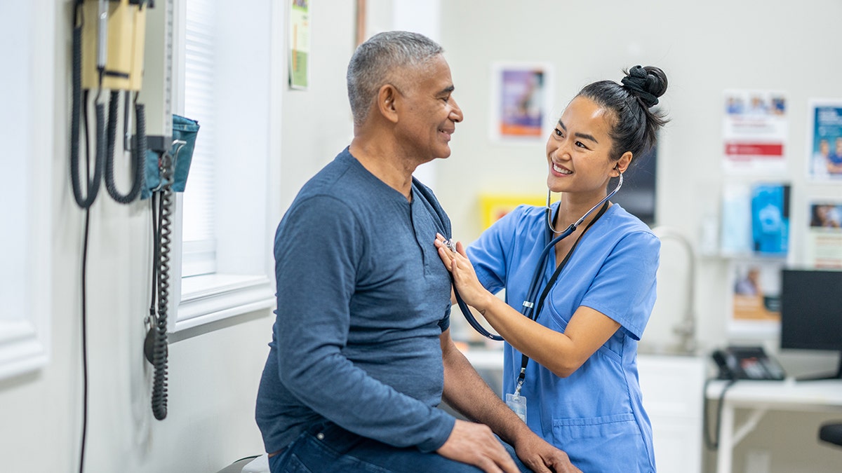 Nurse using a stethoscope to check a male patient’s heartbeat during a medical exam.