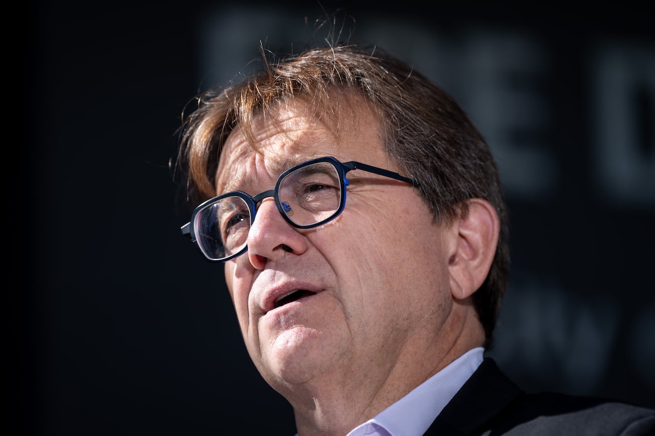 A man wearing rounded square glasses speaks on a sunny day.