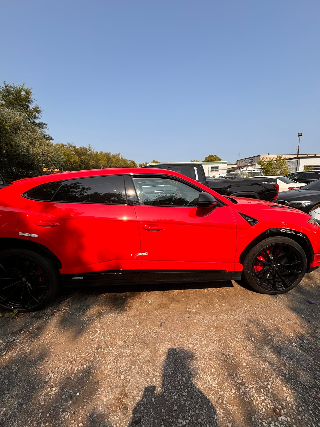 A red luxuy SUV sits parked in a gravel car lot. 