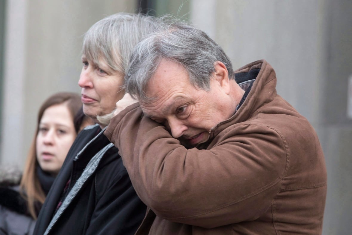 A man wipes his eyes while standing next to a woman at a news conference.