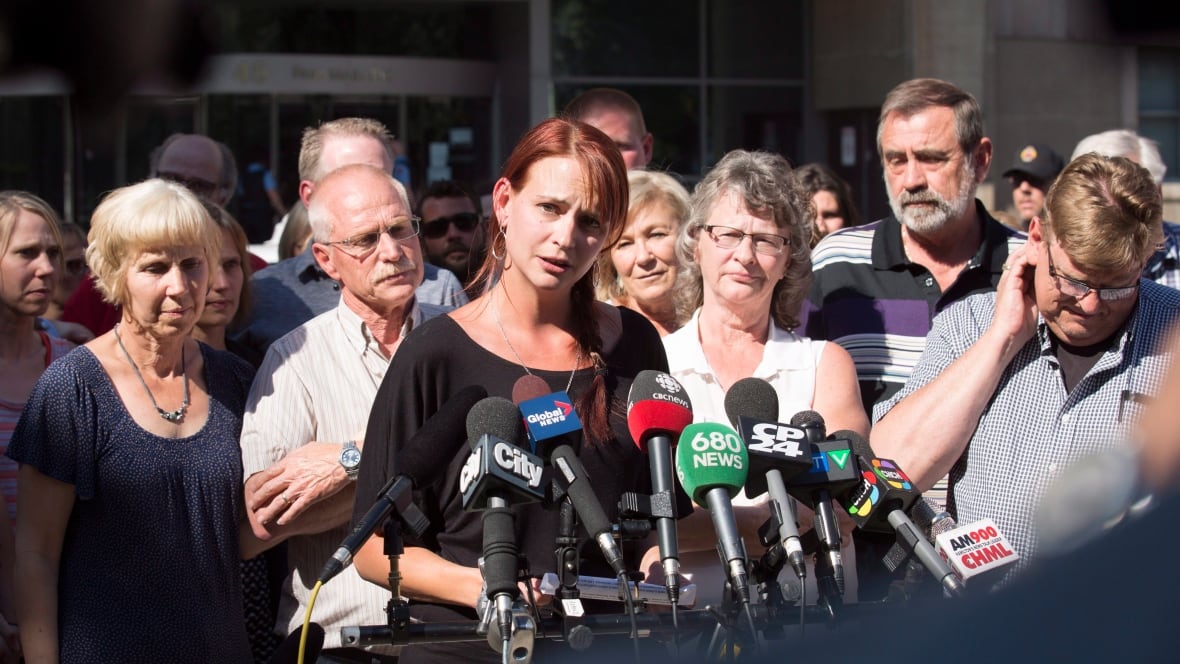 A woman speaks at a press conference, surrounded by supporters.