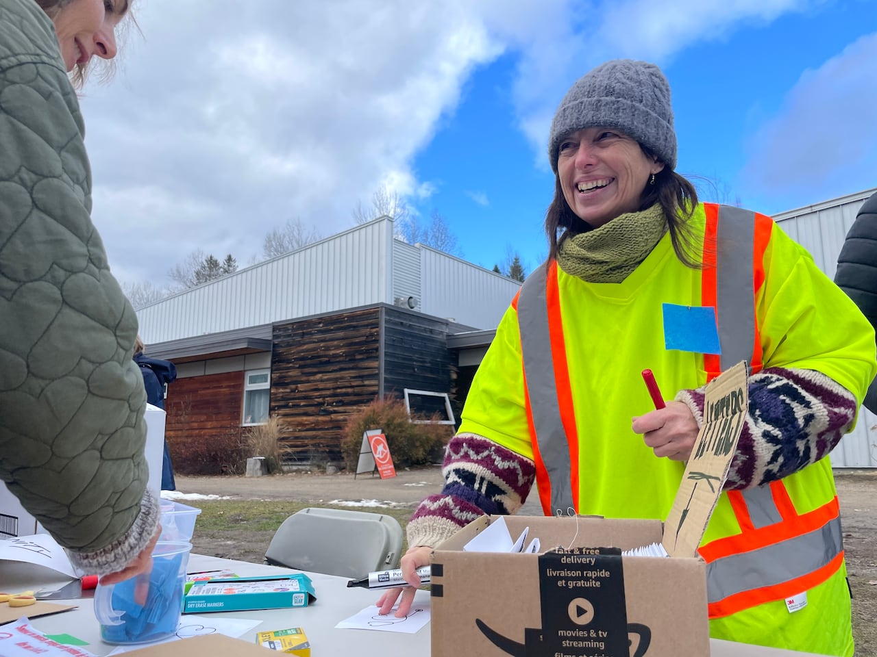 A smiling woman wearing a high vis vest stands at a table of placards