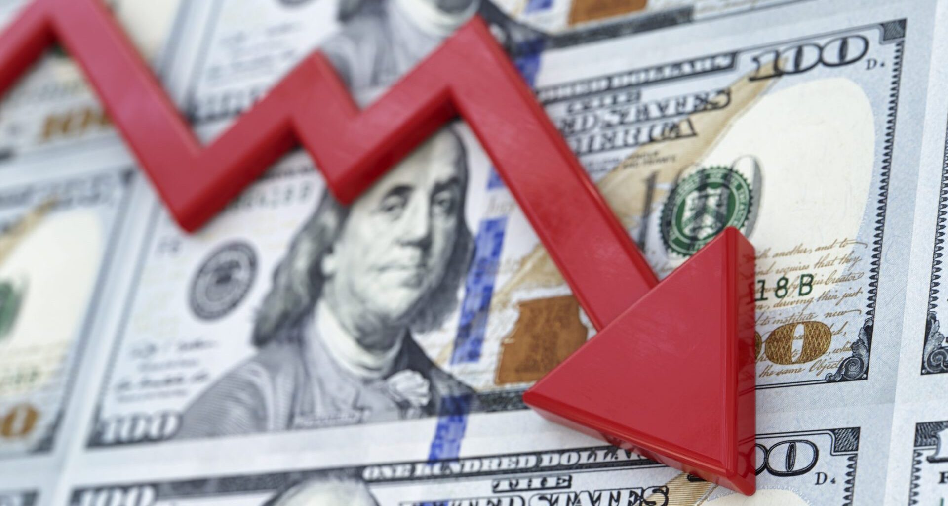 A few one hundred dollar bills with a red arrow on top of it going downward, symbolizing the US economy crashing.