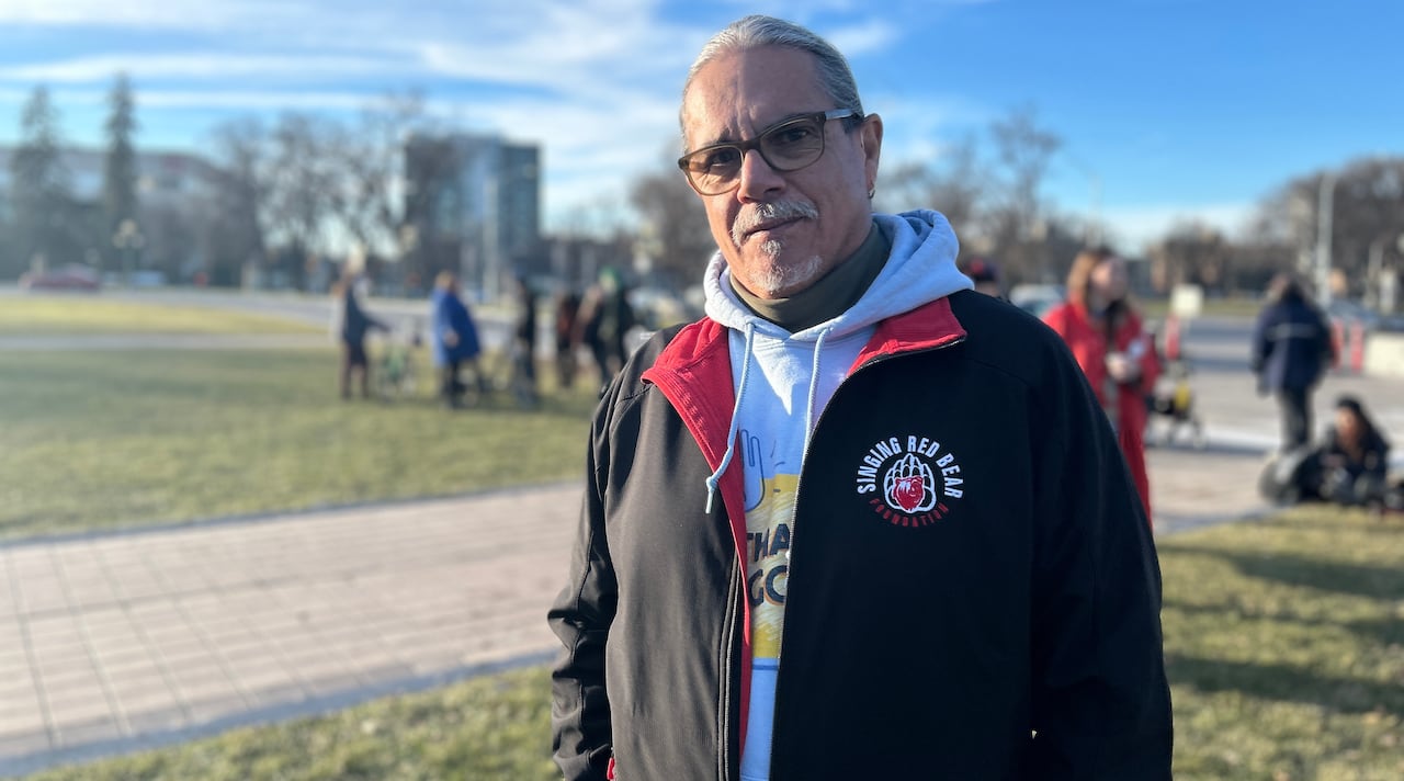 Man wears eyeglasses and a red track jacket with an embroidered logo that reads "Singing Red Bear Foundation"