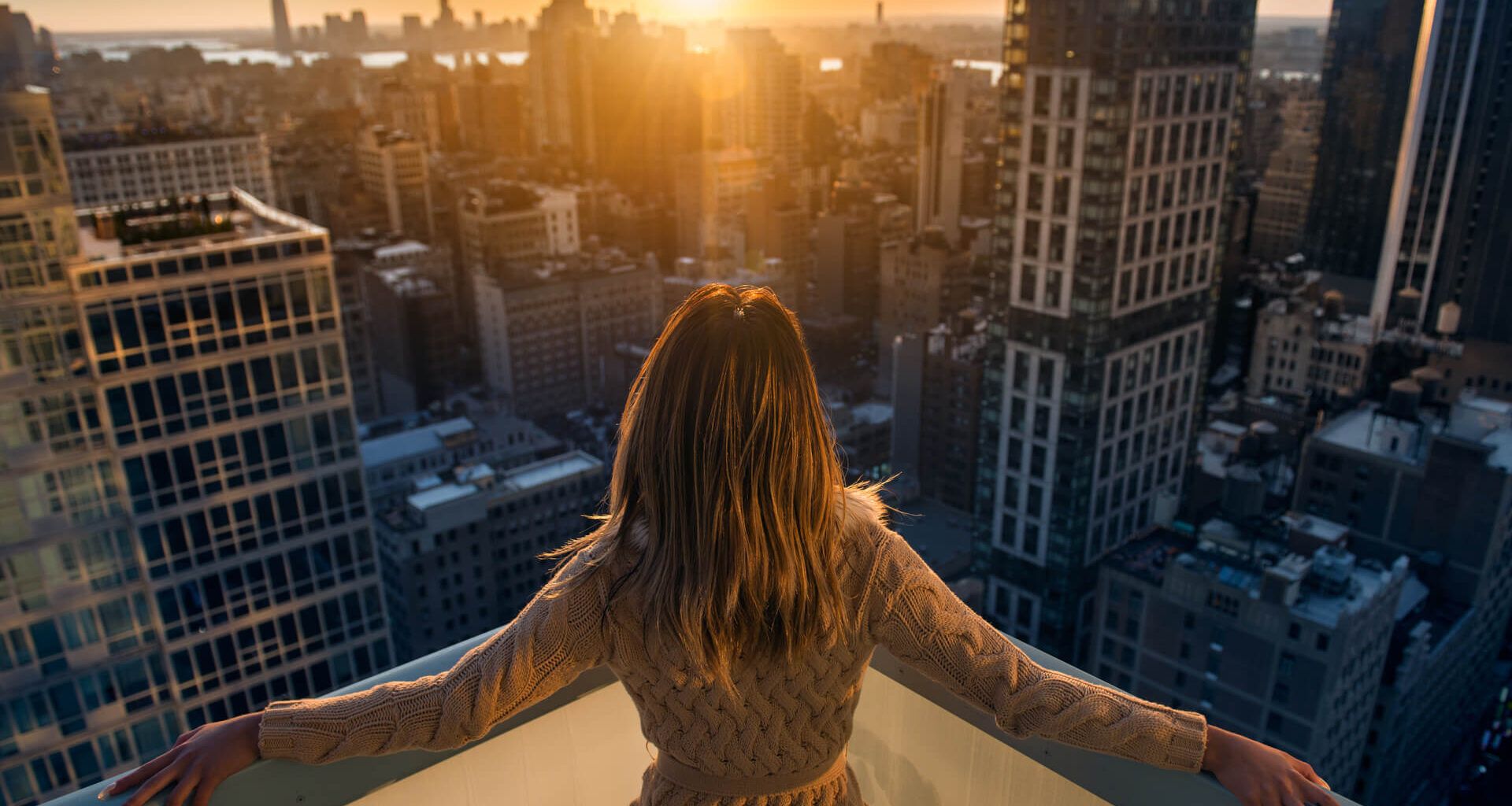 Rich woman enjoying the sunset standing on the balcony at luxury apartments in New York City.
