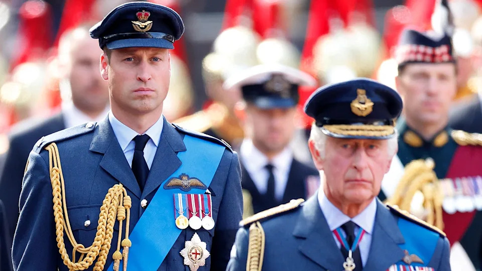 Prince William in a military suit walking behind his father King Charles also in a military suit.