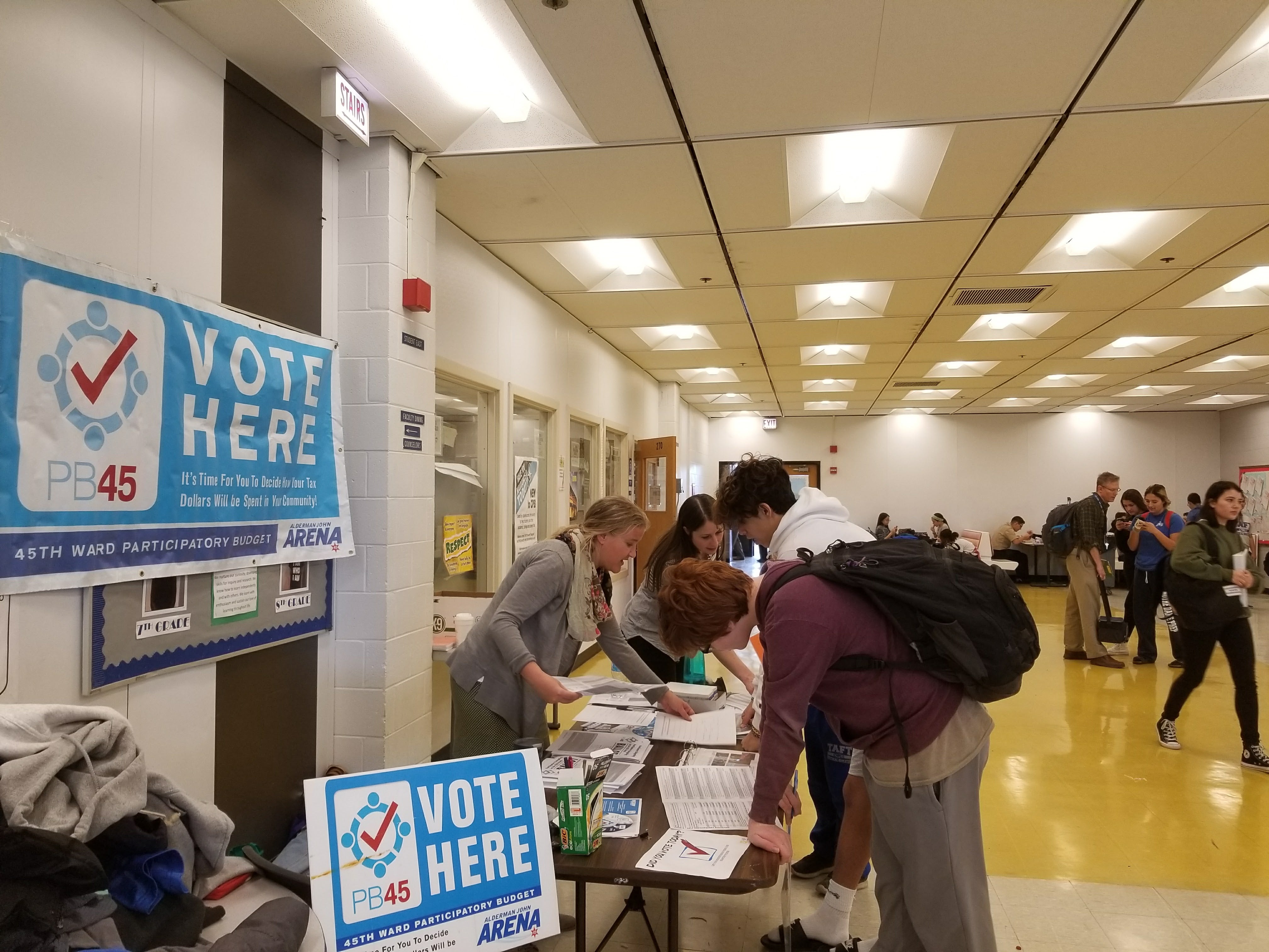 people at a table with "vote here" signs inside a high school