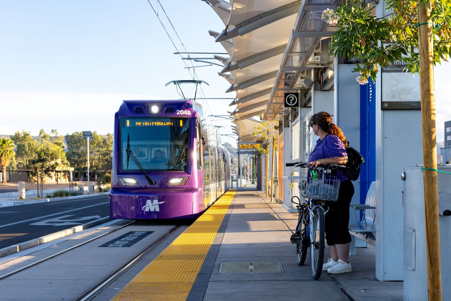 A woman waits for the arriving train at the Baseline/Central Avenue light rail station in Phoenix.