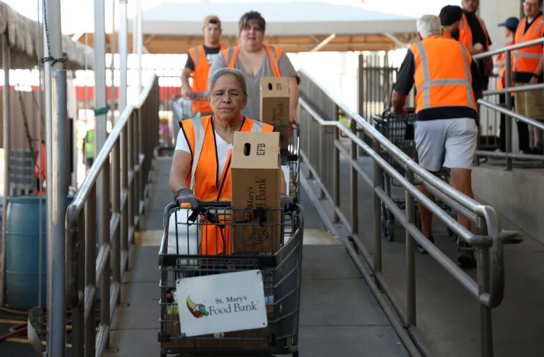 Volunteers Angie Velasquez, front, Jacquie Serr and Andrew Cyber push carts filled with food at St. Mary’s Food Bank in Phoenix on Thursday, Oct. 30, 2025.