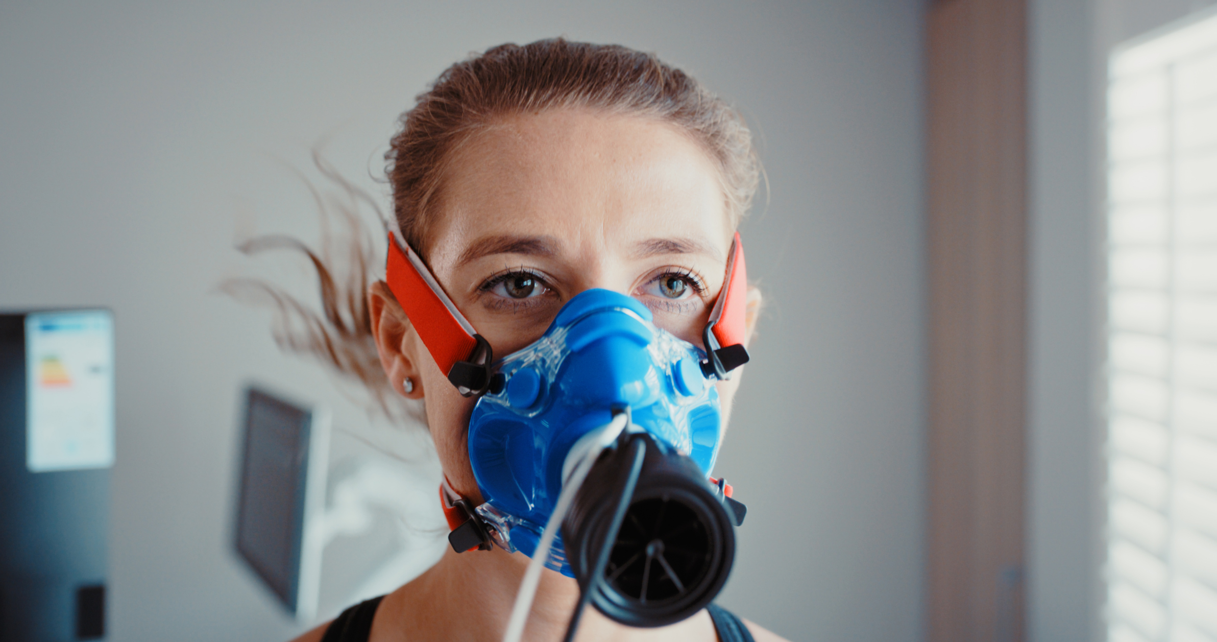 A woman wears a face mask that covers her nose and mouth, white and black leads are connected to the front.