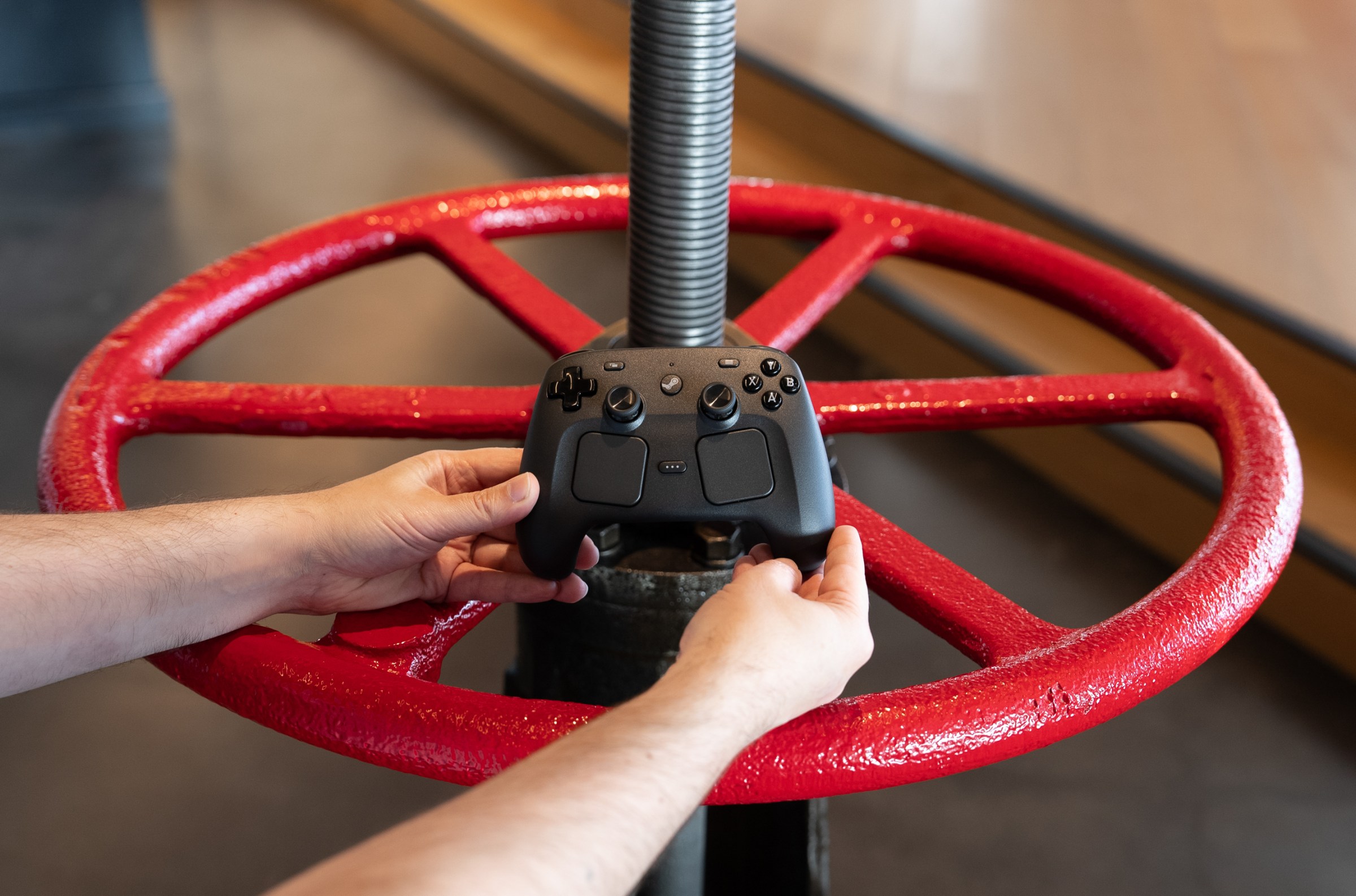 It’s a big red valve, or so it looks, with six spokes on a giant wheeled handle. We’re holding a Steam Controller in front of it.
