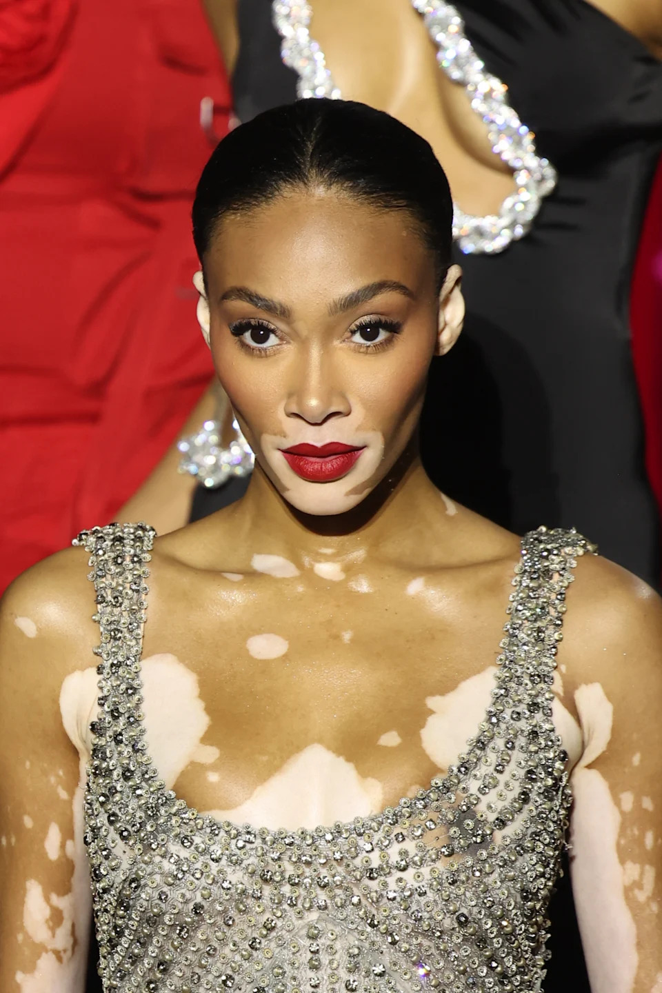 Winnie Harlow wearing a sparkling, embellished gown on the red carpet, exuding elegance with bold makeup and a sleek hairstyle