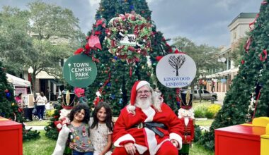kids sit with santa claus in front of a tall christmas tree