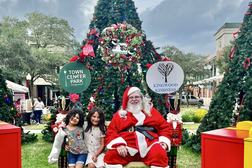 kids sit with santa claus in front of a tall christmas tree