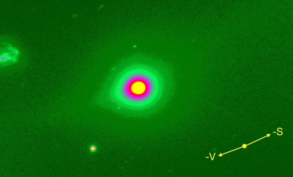 Image of the interstellar comet 3I/ATLAS, showing its nucleus as a bright yellow sphere surrounded by a pink and then green halo, against a dark green background.