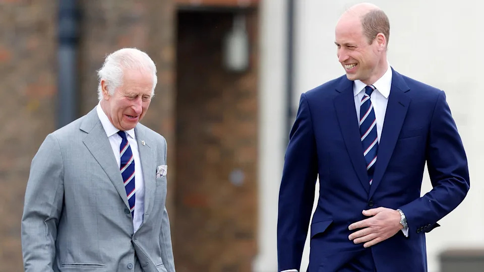 Prince William smiling at a laughing King Charles as they walk together.