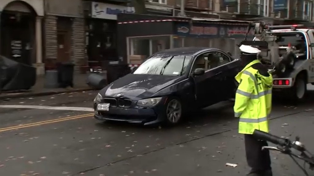 A damaged dark car being towed away on a city street.