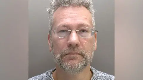 Met Police A mugshot of a man with grey hair and beard and glasses