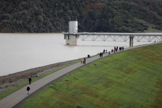 Visitors walk across the top of Coyote Valley Dam as water is released down the spillway at Lake Mendocino near Ukiah, Calif., Monday, January 16, 2023. (Beth Schlanker/The Press Democrat)