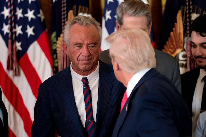 President Donald Trump, shakes hands with Health and Human Services Secretary Robert F. Kennedy Jr. alongside Secretary of Housing and Urban Development Scott Turner (L) after Trump signed the "Fostering the Future" executive order the East Room of the White House on November 13, 2025 in Washington, DC.