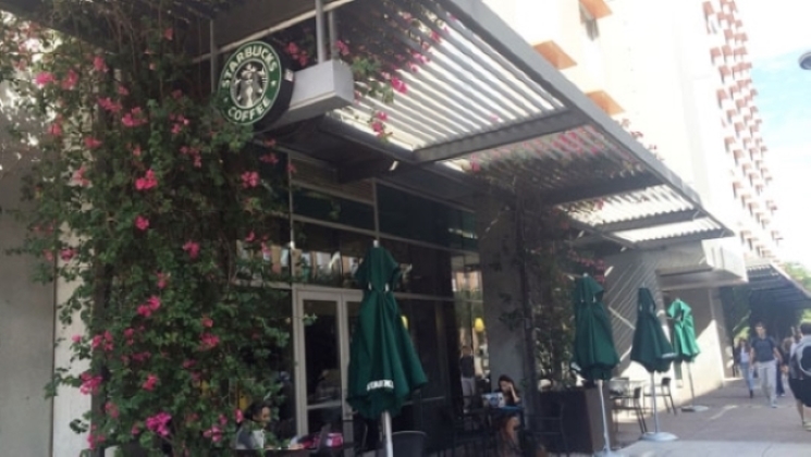 Street view of a Starbucks with flower-covered trellises and outdoor seating.