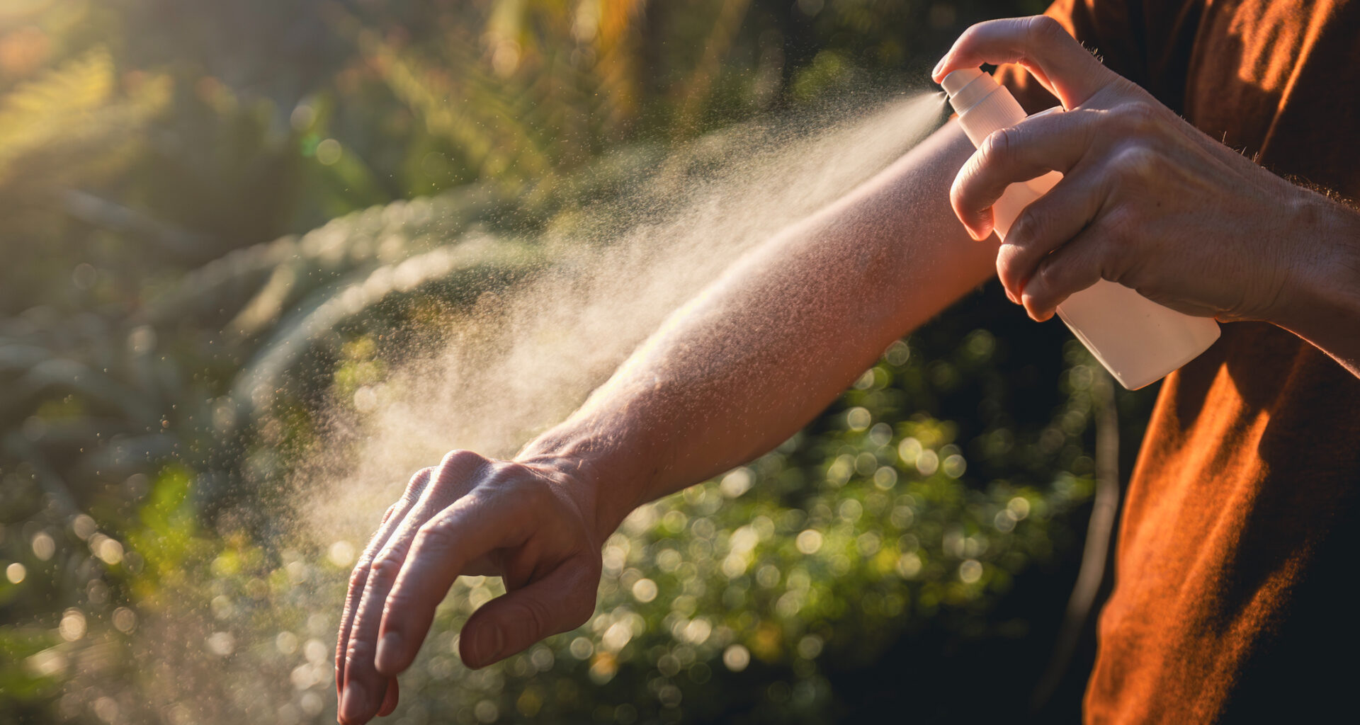 a person sprays bug spray on their arm