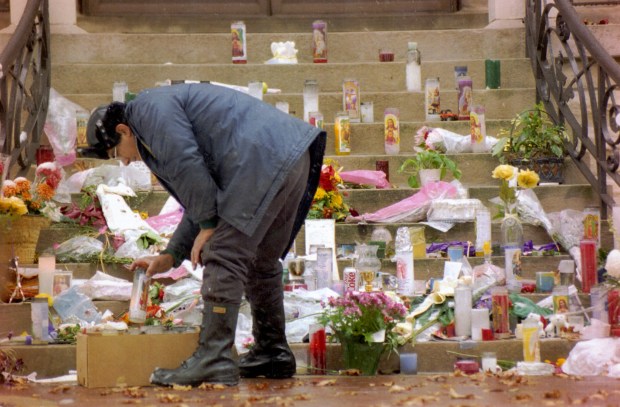 Caretaker Jose Billegas picks up some of the tributes left by well-wishers on the doorstep of the former residence of Cardinal Bernardin after his death, Nov. 21, 1996. The items were taken inside and dried and saved for the Cardinal's family. (Carl Wagner/Chicago Tribune)