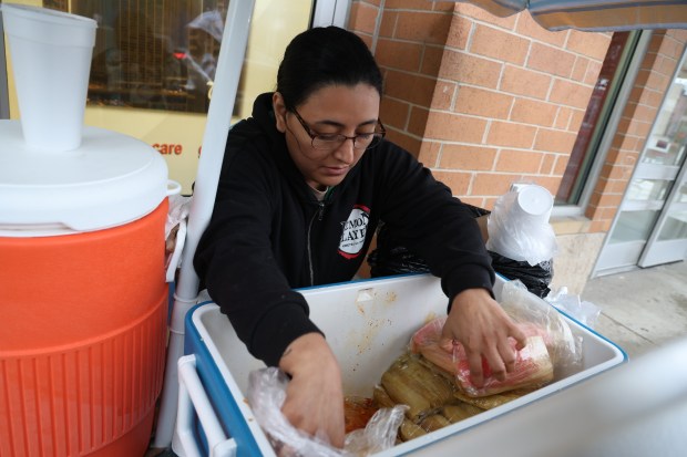 Street vendor Francelia Lagunas retrieves tamales for a customer in Chicago's Avondale neighborhood on Oct. 15, 2025. Lagunas has stepped in selling tamales for another vendor who was detained by federal agents. (Antonio Perez/Chicago Tribune)