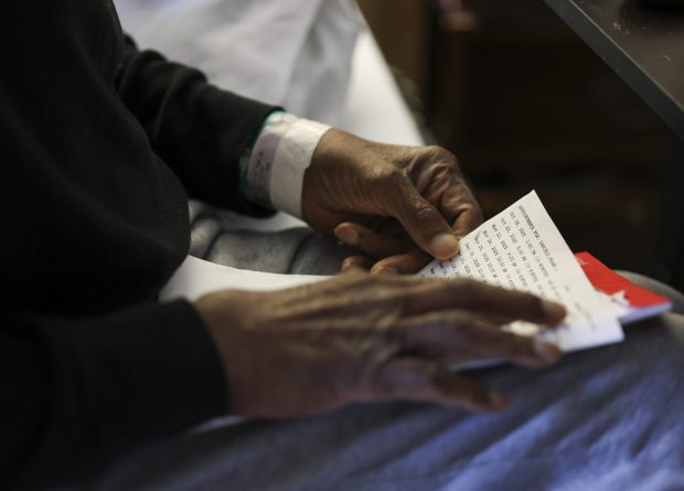 Frank Daniels holds a piece of paper with a list of appointments as he sits on his bed in his nursing home in La Grange Park during a visit with his son, Andre Daniels, on Nov. 13, 2025. Andre is now his father's guardian after many months of guardianship under a private care organization. (Eileen T. Meslar/Chicago Tribune)