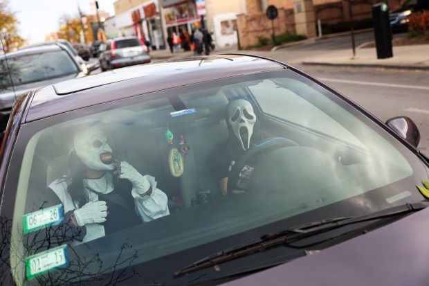 A motorist and passenger wearing masks wait for foot traffic to pass by on West 26th Street in the Little Village neighborhood on Halloween in Chicago, Oct. 31, 2025. (John J. Kim/Chicago Tribune)
