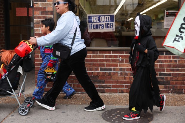 Trick-or-treaters walk past a sign posted at a laundromat that reads "ICE OUT!" on West 26th Street in the Little Village neighborhood on Halloween in Chicago, Oct. 31, 2025. (John J. Kim/Chicago Tribune)