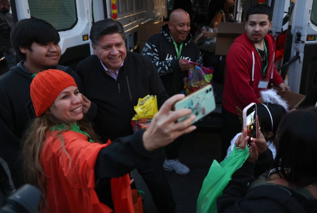 Gov. JB Pritzker takes pictures while handing out candy to trick-or-treaters at a parking lot on West 26th Street in the Little Village neighborhood of Chicago on Halloween. (John J. Kim/Chicago Tribune)
