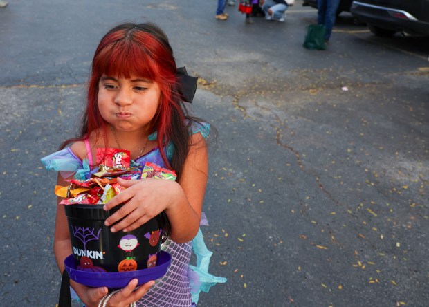 Jayla Carrera, 7, tries not to spill candy after going through the the trick-or-treat line on Halloween in West Chicago on Oct. 31, 2025. Members of the West Chicago Angels and Christ Our Advocate Church along with students from Wheaton College organized a safe trick-or-treat event for families who reside in areas heavily targeted by federal agents. (Stacey Wescott/Chicago Tribune)