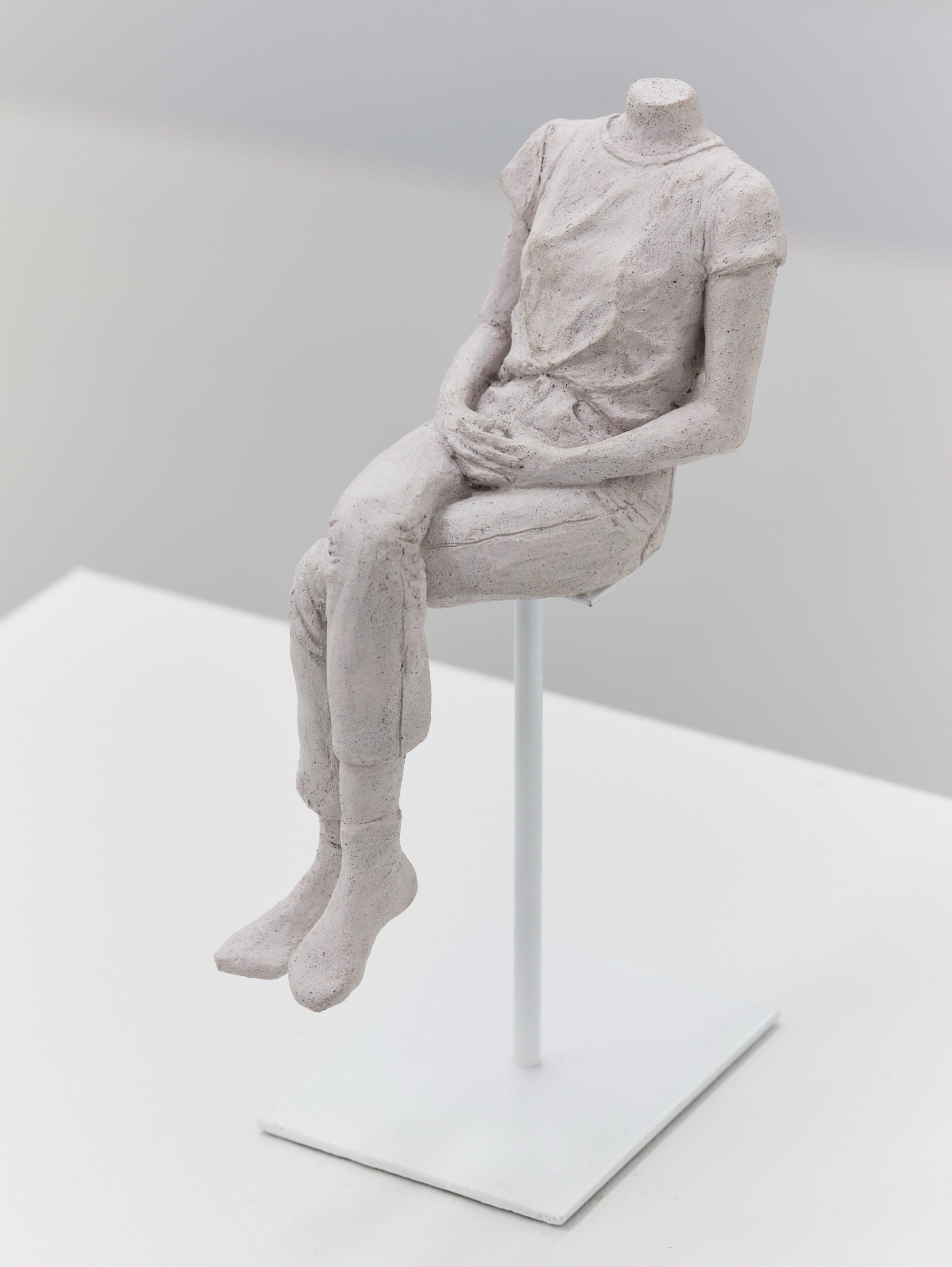 a ceramic sculpture by Léonore Chastagner of a seated female figure, wearing jeans and a t-shirt, with legs crossed and without a head
