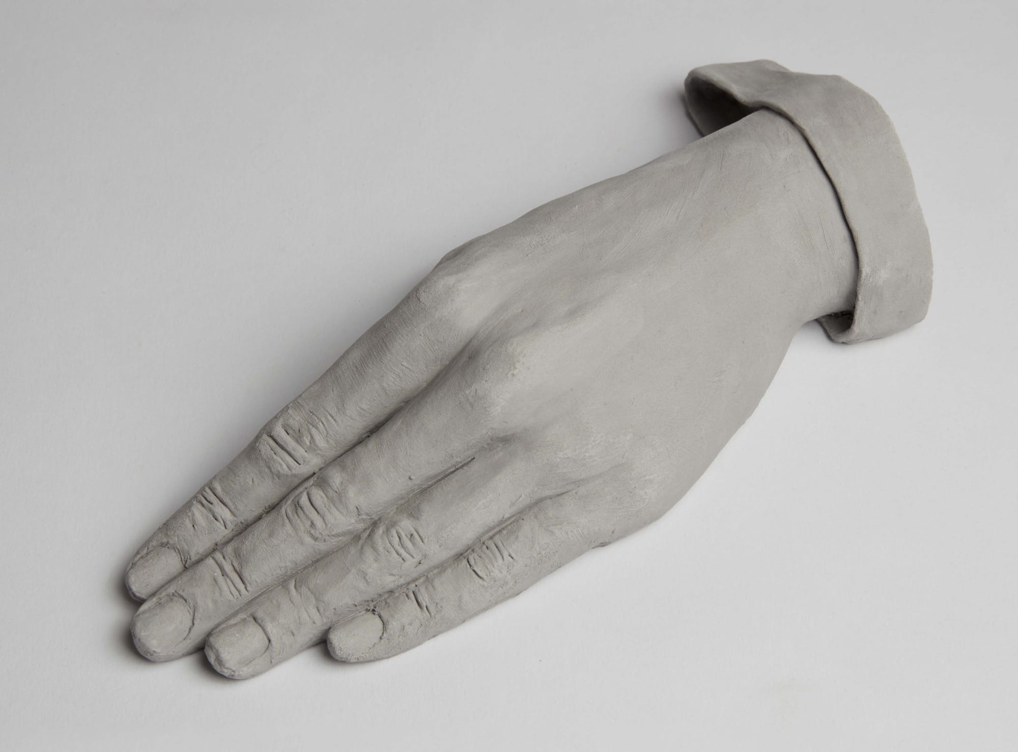 a ceramic sculpture by Léonore Chastagner of a slender hand and detail of a sleeve, made in light gray clay