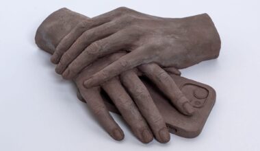 a clay sculpture by Léonore Chastagner of two hands folded over a smartphone