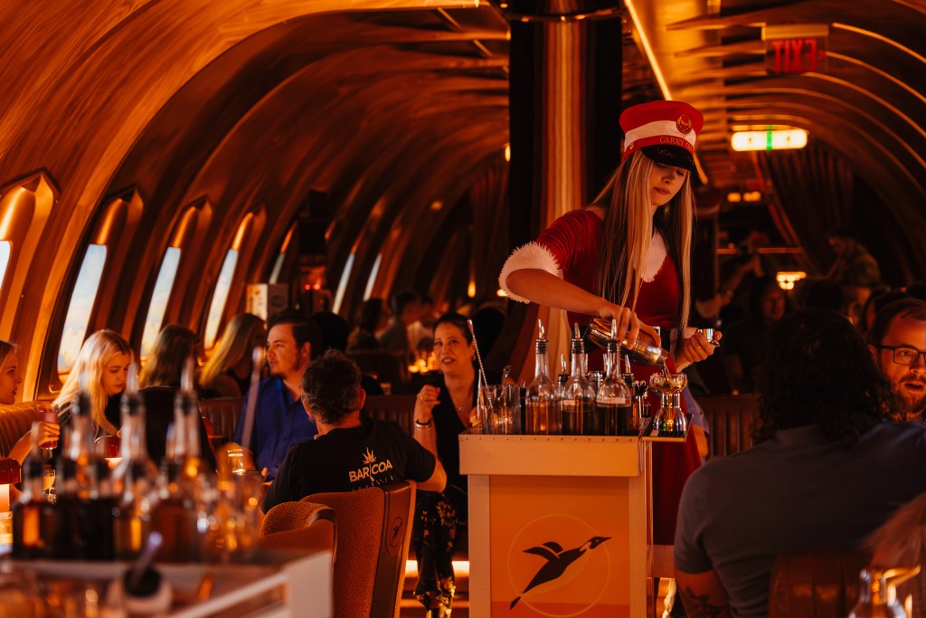 A woman dressed in a Santa suit pours martinis at a holiday-themed bar.
