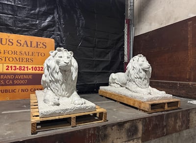 Two concrete lions sit on two wooden pallets.