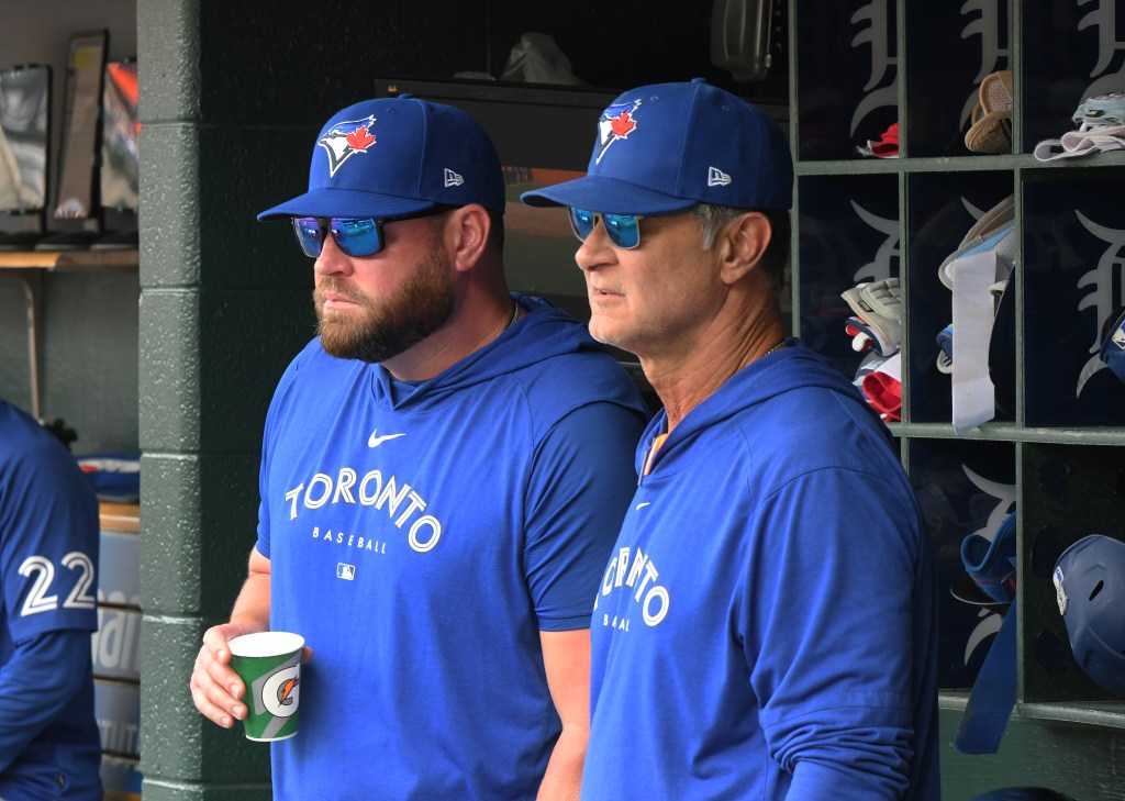 Two men in Toronto Blue Jays baseball caps and shirts in the dugout.