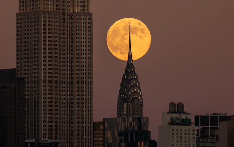 The full Beaver Supermoon rises behind the Chrysler Building and the Empire State Building in New York City