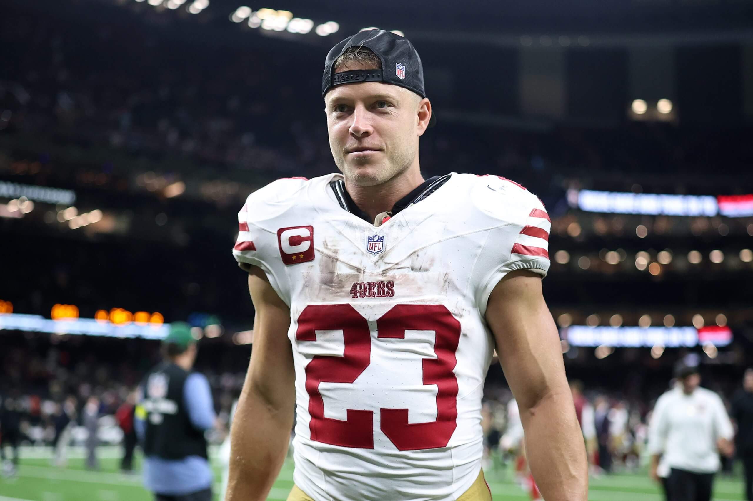 Christian McCaffrey, wearing a white No. 23 uniform and a backward hat, has a light smile on his face while walking off the field after a win in New Orleans.