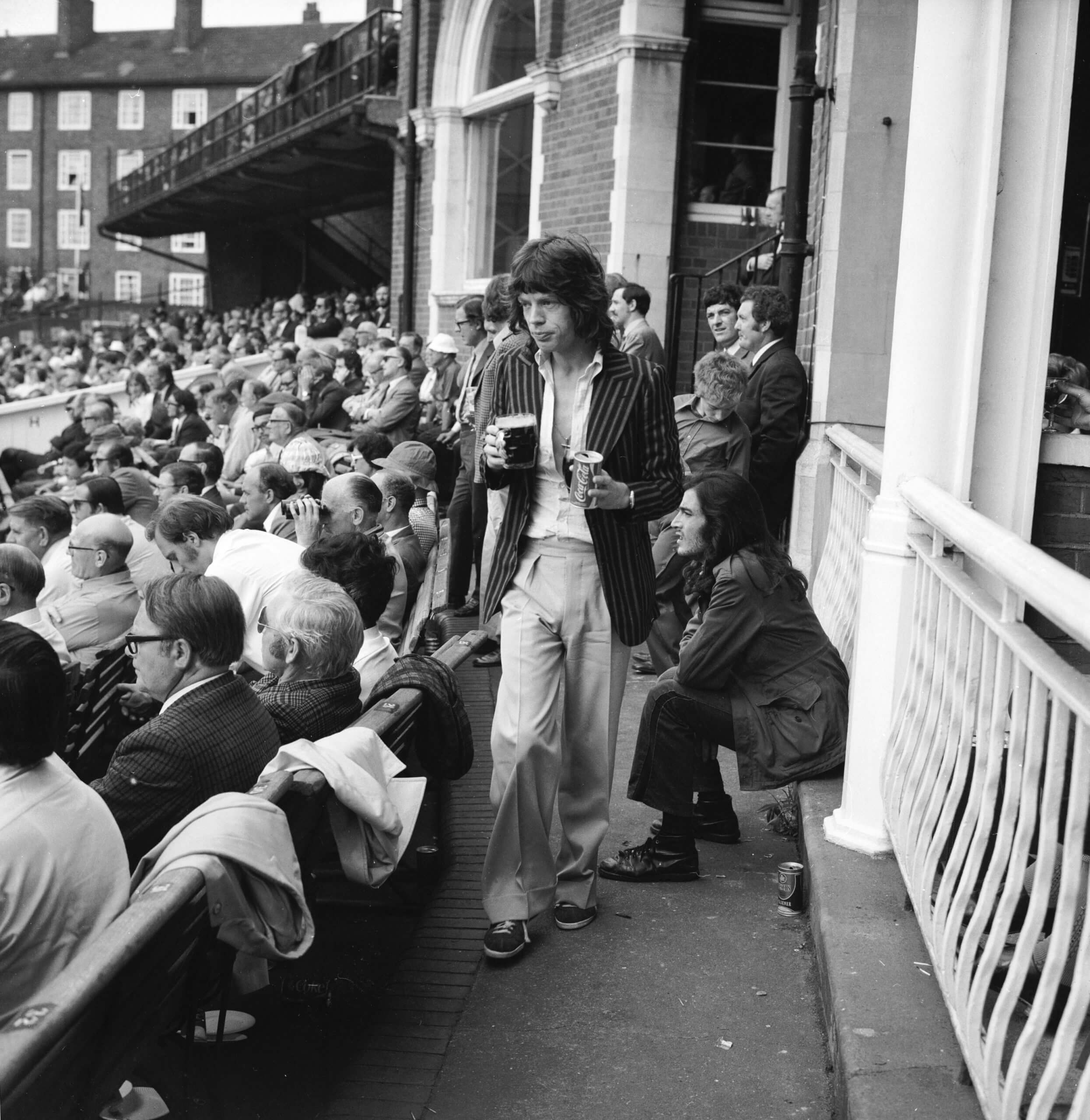 A young Mick Jagger, clasping a pint and a can of Coke, returns to his seat at The Oval in London to watch England take on Australia in August 1972